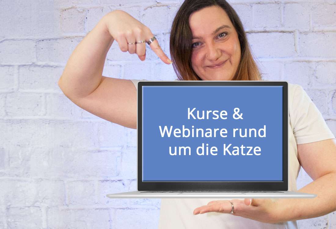 Eine brünette Frau im weißen T-Shirt mit Aufdruck katzen-fieber.de formt mit den Fingern ein Herz