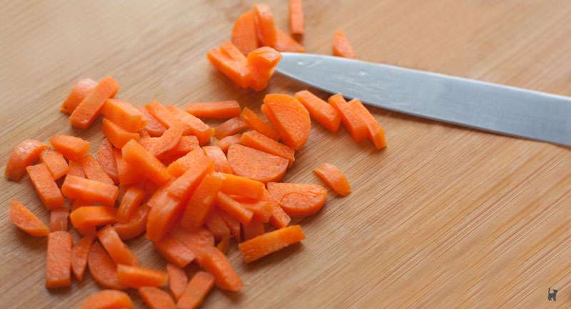 Das Foto zeigt ein Holzschneidebrett, auf dem kleingeschnittene Karotten und ein Messer liegen