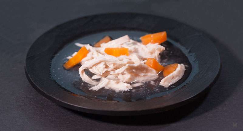 Das Foto zeigt einen kleinen Teller, der mit Brühe, Hähnchen- und Karottenstücken gefüllt ist
