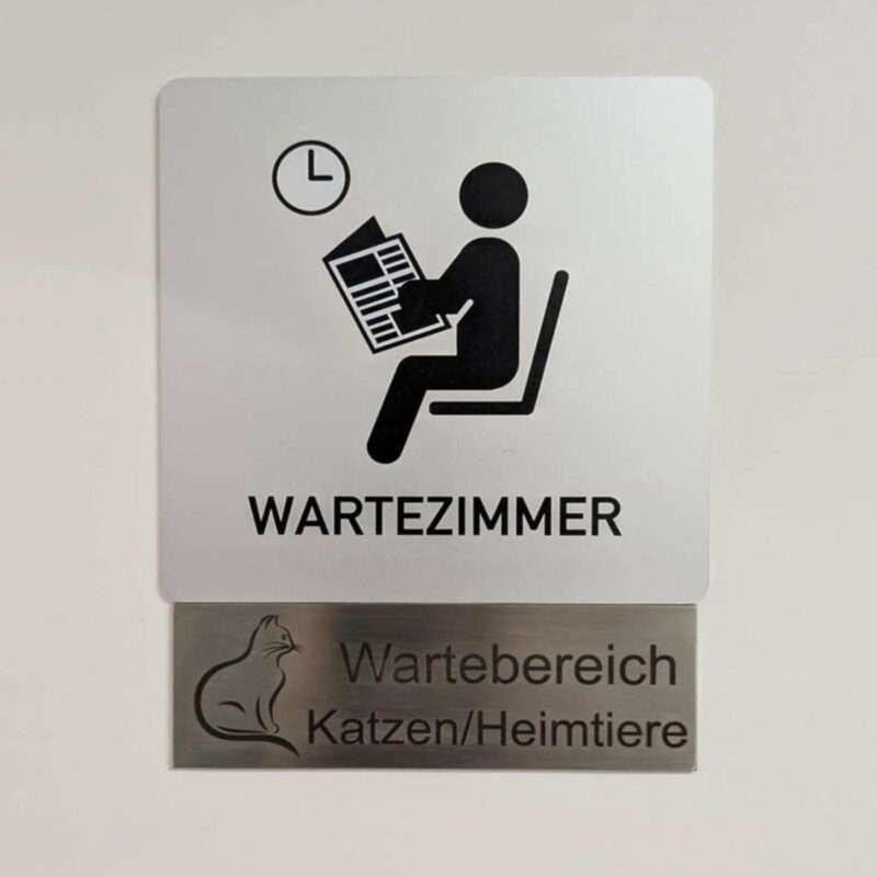 Das Foto zeigt eine Tür, an der zwei Metallschilder hängen. Die Aufschrift der Schilder sagt "Wartezimmer - Wartebereich Katzen / Heimtiere"