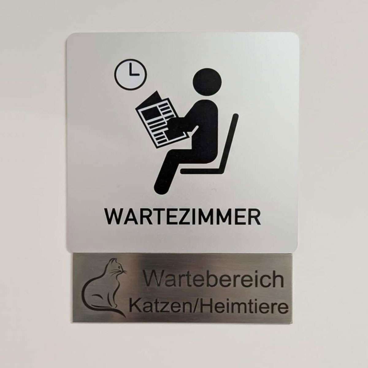 Das Foto zeigt eine Tür, an der zwei Metallschilder hängen. Die Aufschrift der Schilder sagt "Wartezimmer - Wartebereich Katzen / Heimtiere"
