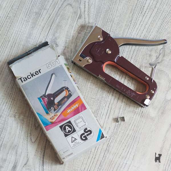 Auf dem Foto liegt ein Handtacker auf einer Oberfläche. Neben ihm liegen die Verpackung und passende Tackernadeln.